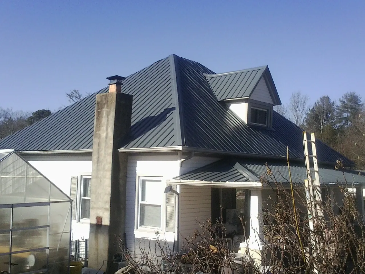 Dark blue standing seam metal roof on a white farmhouse with dormer — Slate & Tile Roof Repair by Roofing Brothers in Mineola