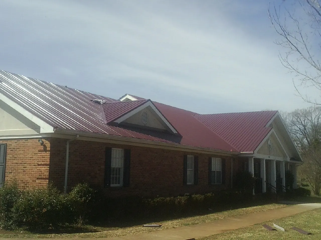 Red metal roof with gabled entries on a long brick building, from a Hail Damage Roof Repair job in Mineola