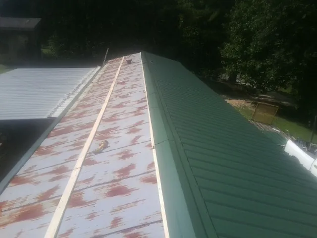 Old rusted panels beside newly installed green metal roofing — Wind Damage Roof Repair by Roofing Brothers in Mineola