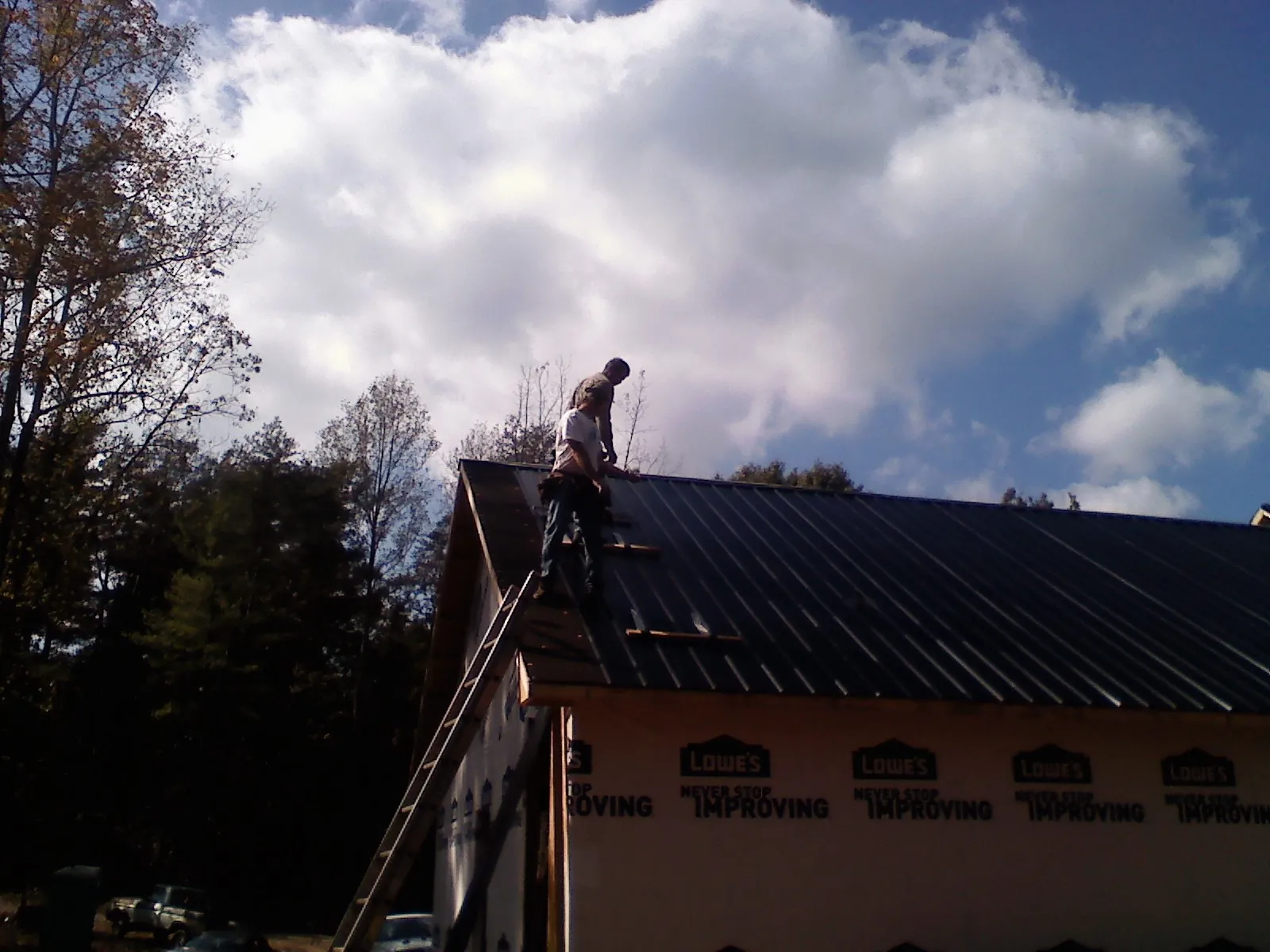 Roofer fastening dark metal panels high against a cloudy sky, from a Roof Inspection job in Mineola