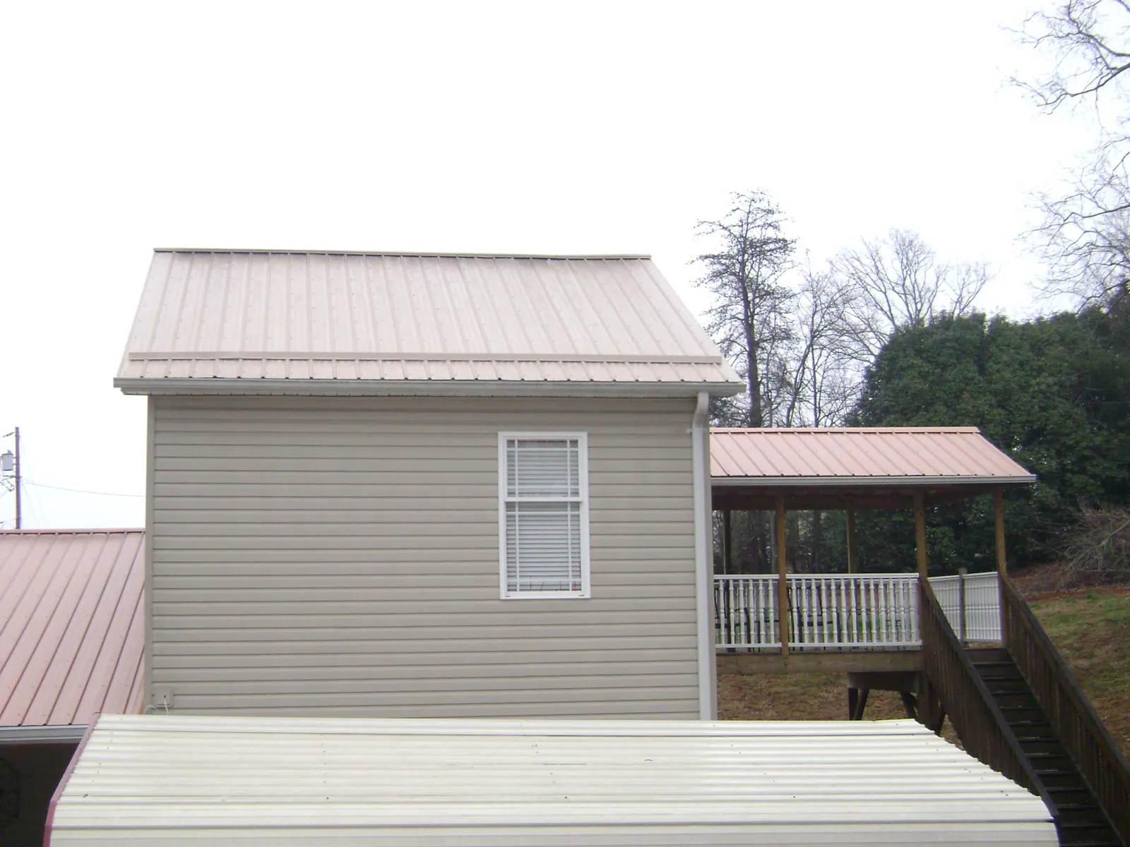 Tan metal roofs on a two story addition and attached porch, from a Roof Replacement job in Mineola