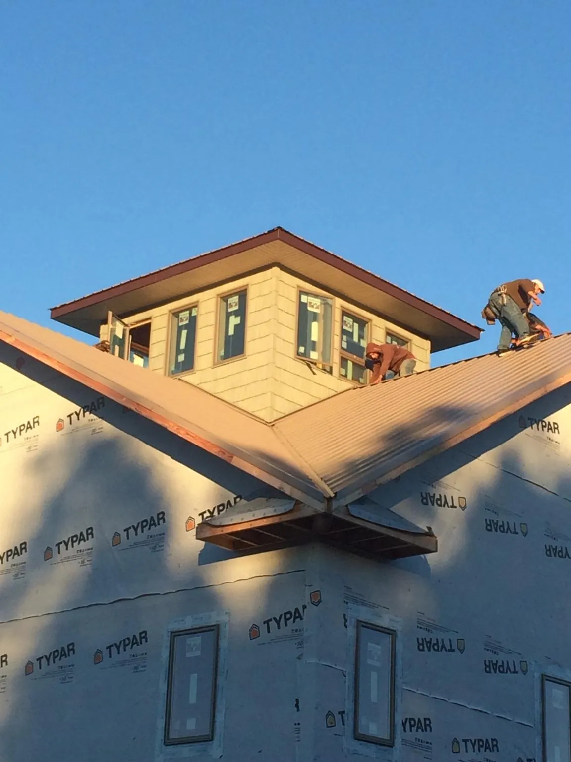 Roofers working around a rooftop cupola on a new metal roof at sunset — Roof Waterproofing in Mineola by Roofing Brothers